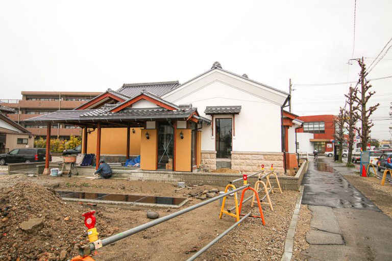 オレンジと白の和風建築の施設外観。庭には砂利敷きと自転車ラックがある。